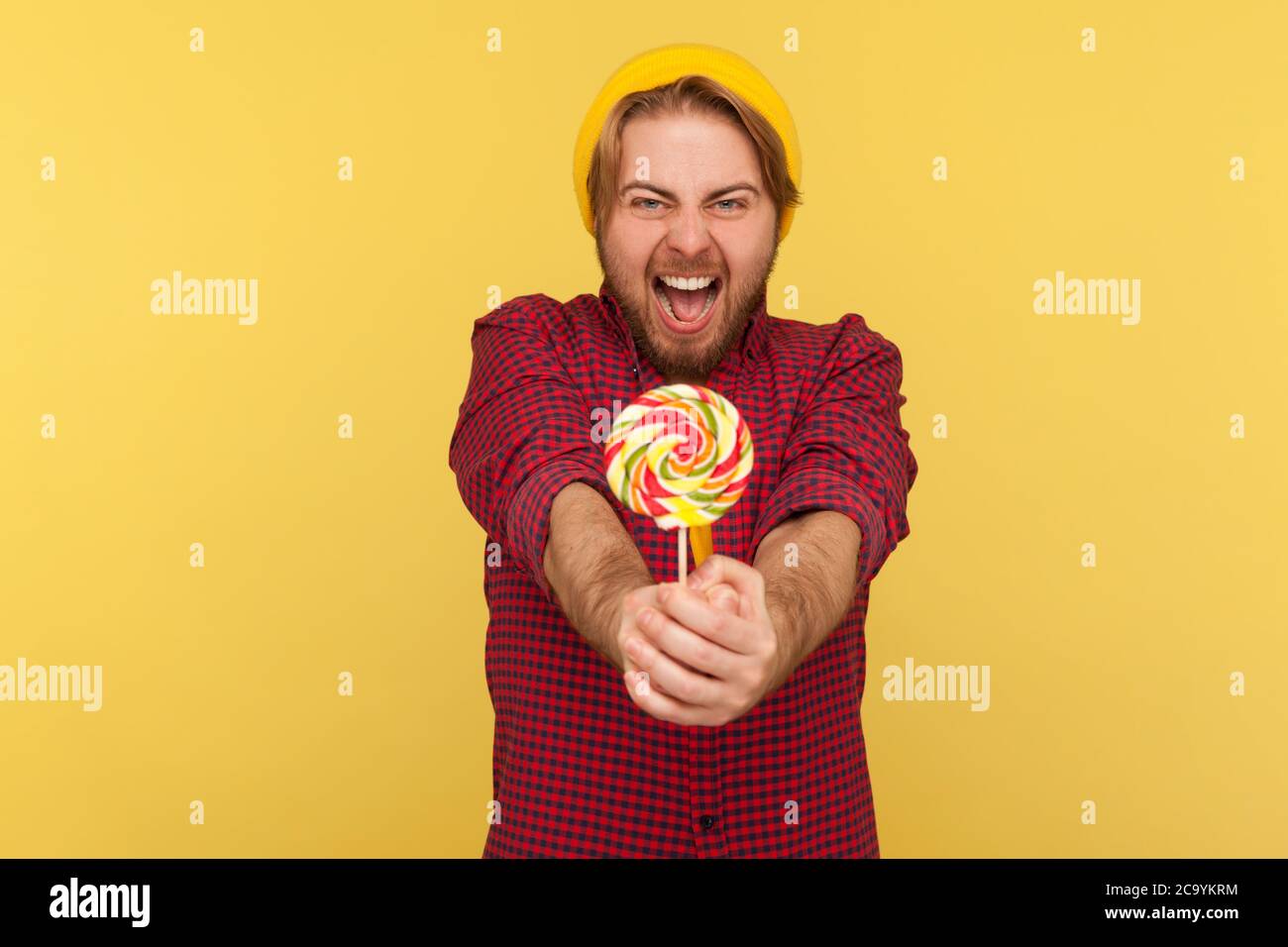 Extrem fröhlich entzückter Hipster Kerl in Beanie Hut, kariertes Shirt geben Lollipop an die Kamera und schreit vor Aufregung, verrückt nach süßem Zucker Stockfoto