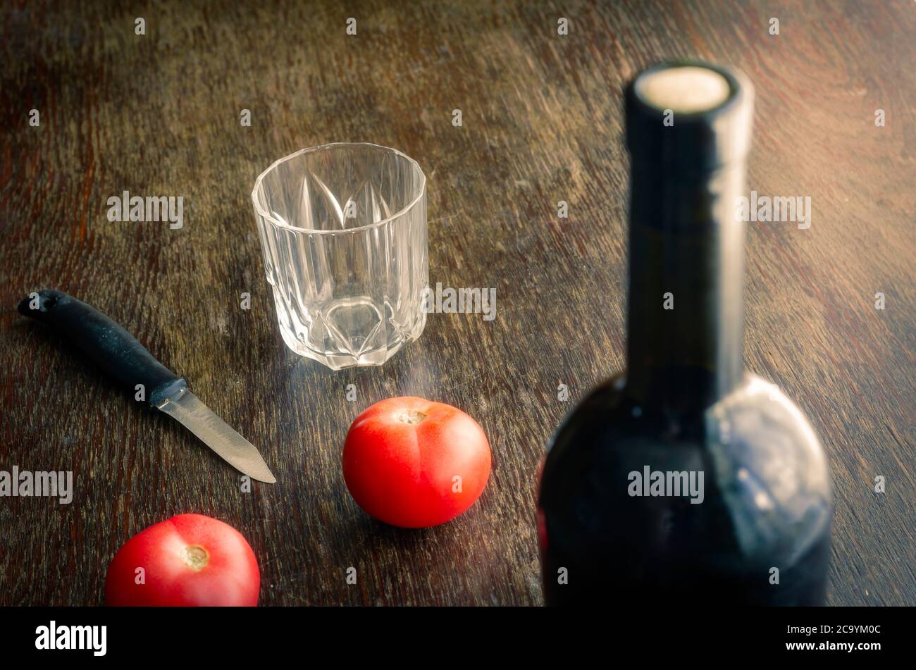 Versiegelte Flasche Rotwein auf Holztisch mit reifen Tomaten. Volle Flasche Wein mit Kork, zwei roten Tomaten, Messer und ein leeres Glas. Konzentrieren Sie sich auf Stockfoto