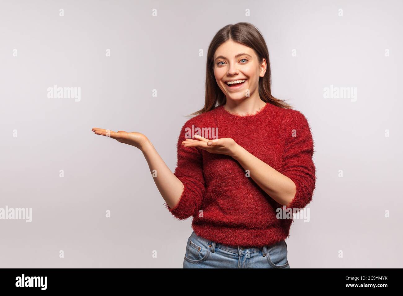 Seht hier, wirbt! Portrait von glücklich hübsches Mädchen in zotteligen Pullover hält leeren Raum auf ihren Handflächen, leere Wand für kommerzielle Idee, Produktbild. Stockfoto