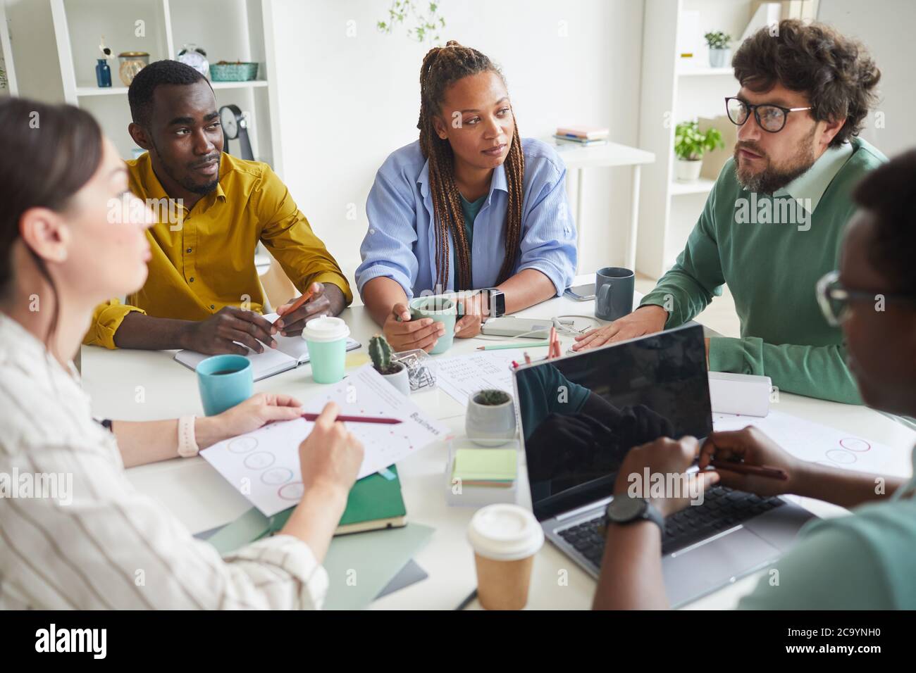 Porträt eines modernen multiethnischen Teams, das Geschäftsprojekt diskutiert, während man an einem überladen Tisch im Konferenzraum sitzt und dem Manager zuhört, um Platz zu kopieren Stockfoto