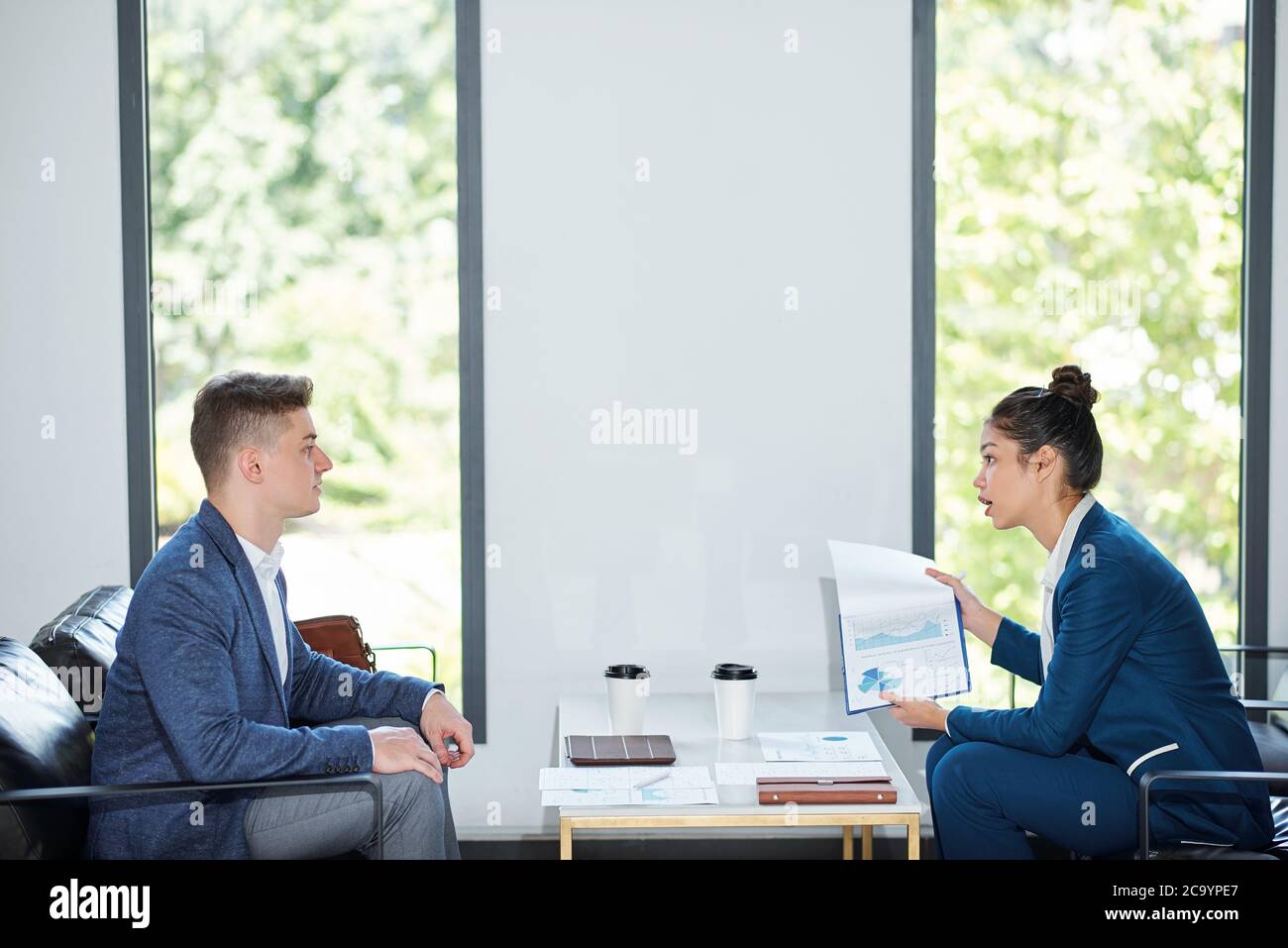 Seriöse junge Geschäftsfrau zeigt Finanzbericht an Employee und erzählt ihm aus für schlechte Zahlen Stockfoto