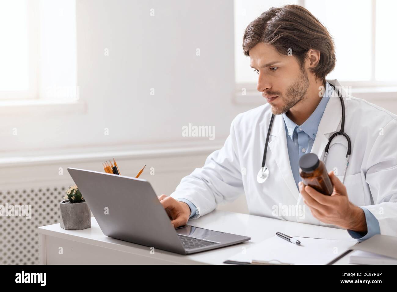 Junger Arzt liest Anleitung für Pillen auf Laptop Stockfoto