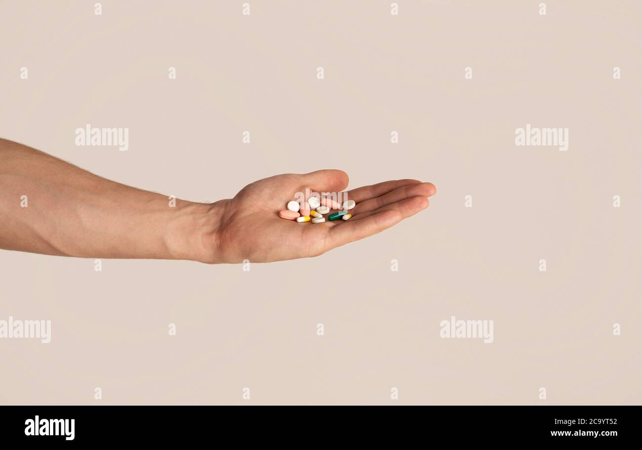 Unerkennbarer junger Kerl hält Haufen Pillen in der Hand über hellen Hintergrund, Nahaufnahme Stockfoto