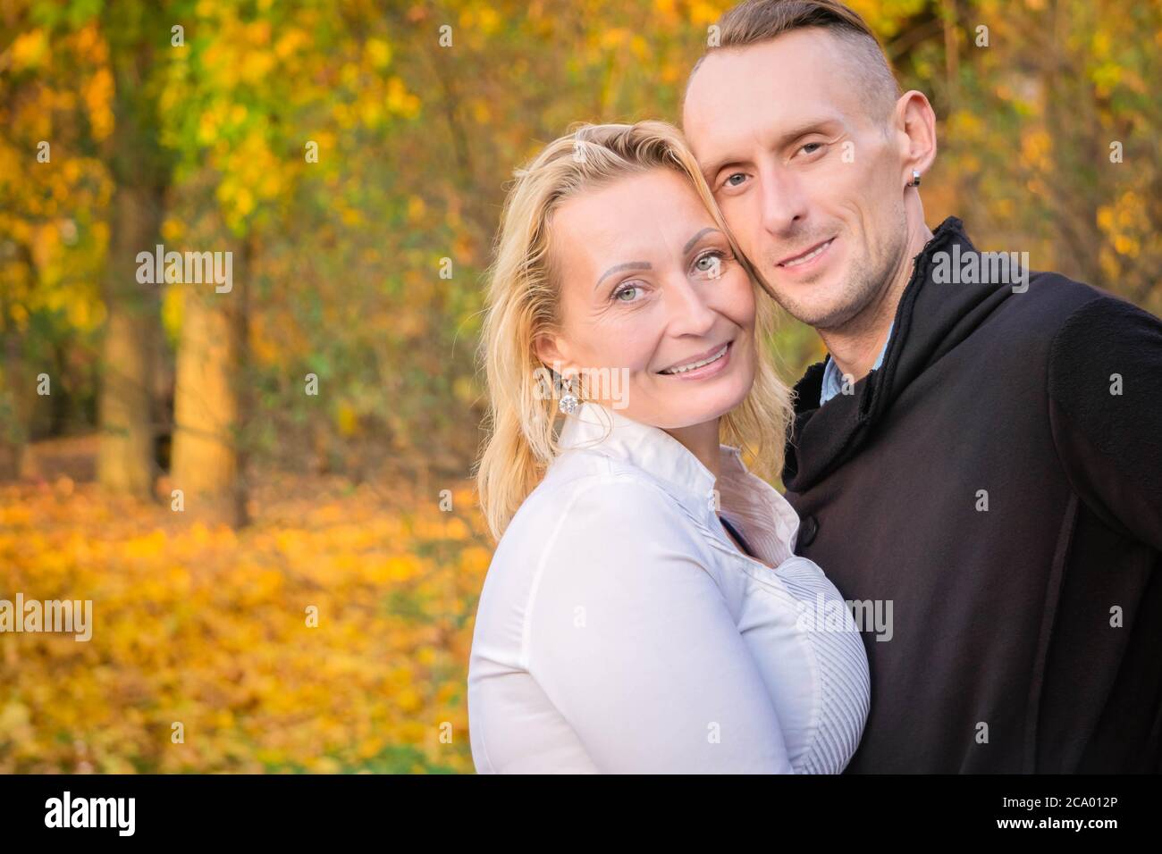Schönes Paar mittleren Alters im Herbstpark. Lächelnder Mann und Frau umarmten sich vor dem Hintergrund des Sturzes. Pärchen Spaß im bunten Herbstpark. Glückliches Paar auf fa Stockfoto