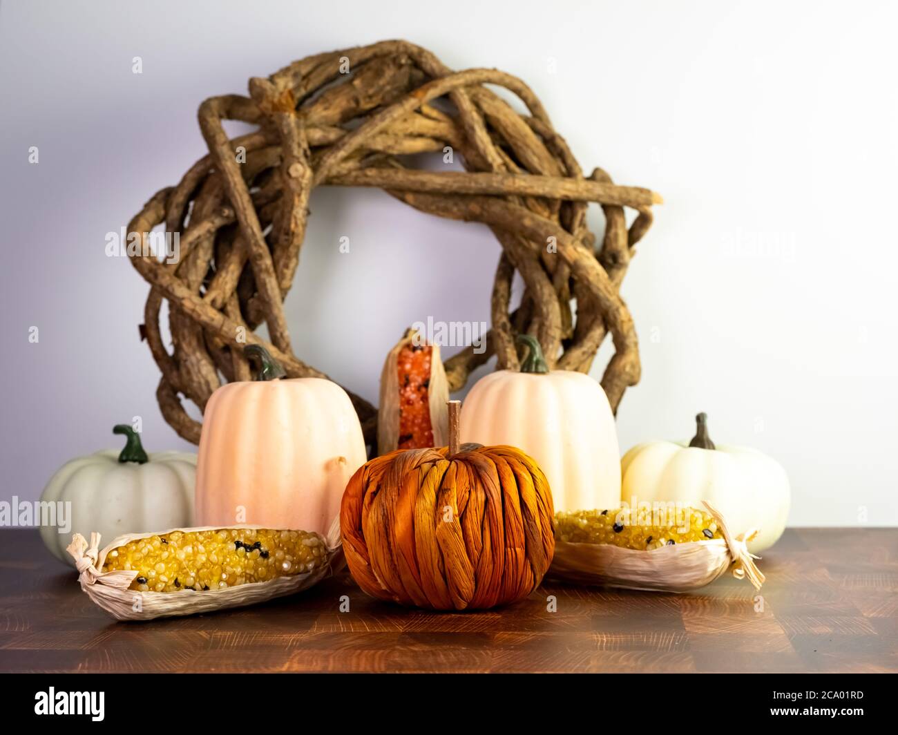 Herbst-Dekor, ein Holzkranz mit kleinen Kürbiskürbis Kürbis Kürbis und Herbst Mais mit einem orangen Kürbis in der Mitte auf einer Holzoberfläche mit einer weißen Wand Stockfoto