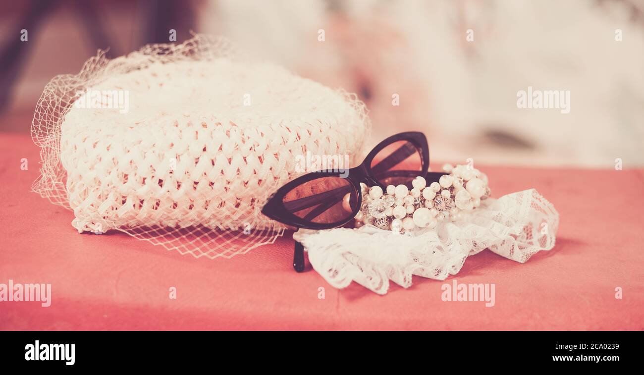 60er Jahre Hut mit Spitze mit Perlen und Cat Eye Sonnenbrille auf rosa Koffer Stockfoto