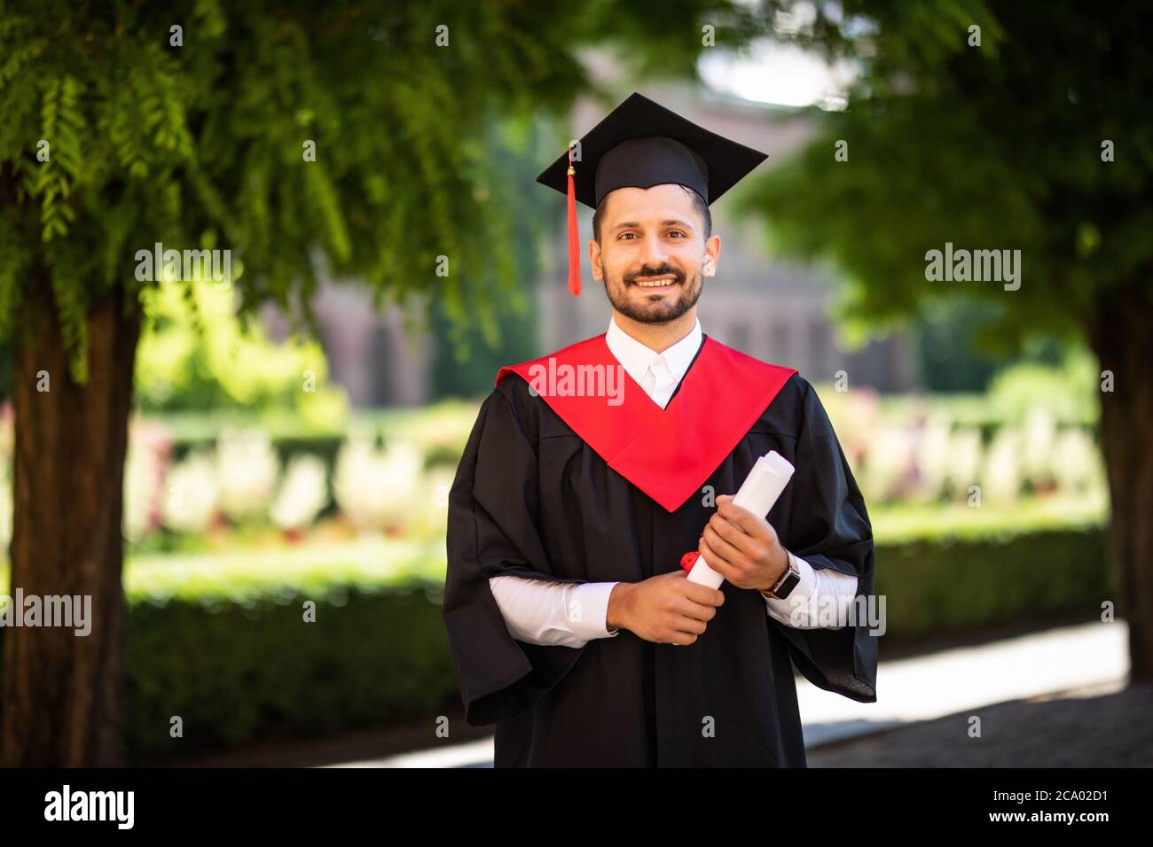 Junge männliche Student in schwarzen Abschlusskleid gekleidet. Campus als Hintergrund. Stockfoto