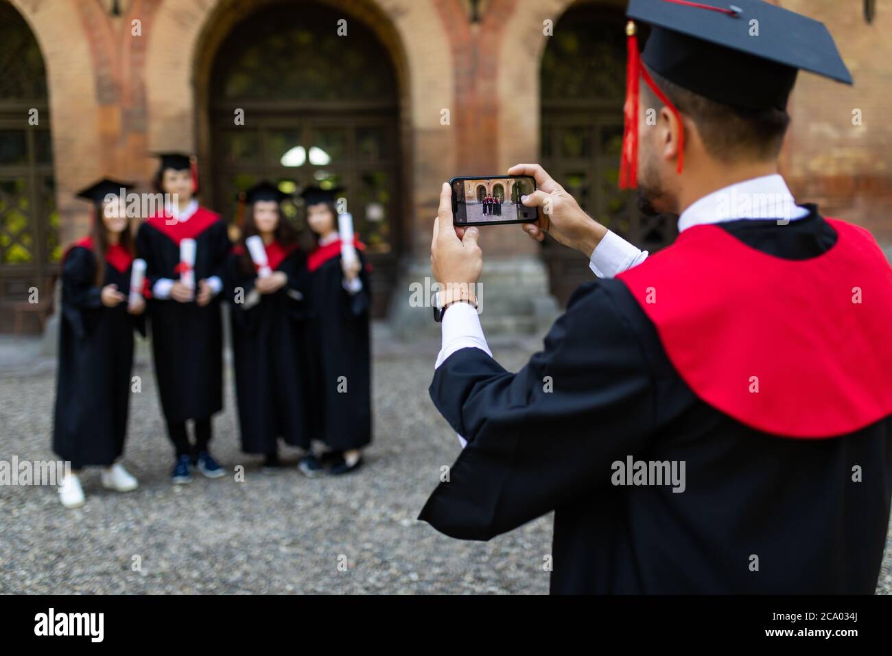 Junge Graduiertenstudenten fotografieren nach der Zeremonie am Telefon auf dem Campus Stockfoto