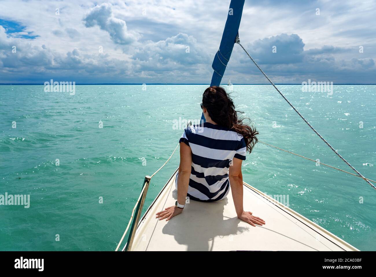 Frau, die auf einem Segelboot auf dem Plattensee auf dem Schiff sitzt, genießt die Freiheit Stockfoto