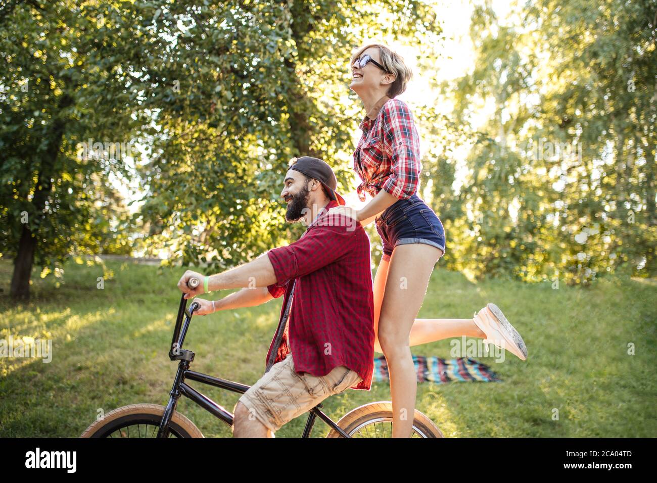 Kaukasische fröhliche Paar Reiten ein Fahrrad im öffentlichen Park in ihrer Freizeit und Spaß am sonnigen Sommertag. Stockfoto Kaukasische fröhliche Paar Reiten ein Fahrrad im öffentlichen Park in ihrer Freizeit und Spaß am sonnigen Sommertag. Stockfoto