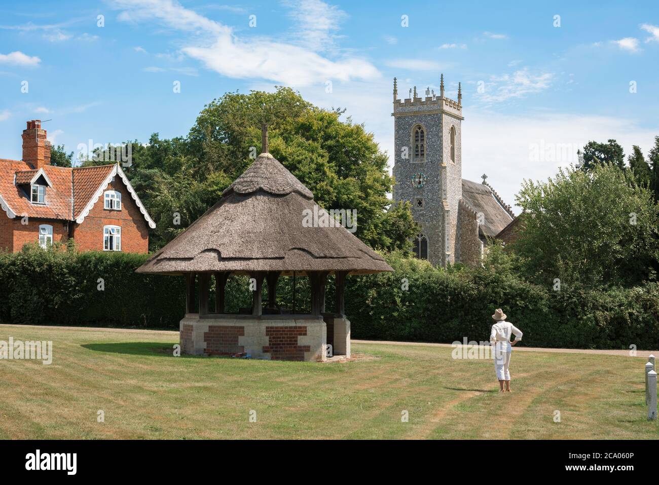 England Land Sommer, Blick auf eine alleinreisende Frau auf einem typischen englischen Dorf grün stehen und Blick auf eine nahe gelegene Kirche, Norfolk UK Stockfoto