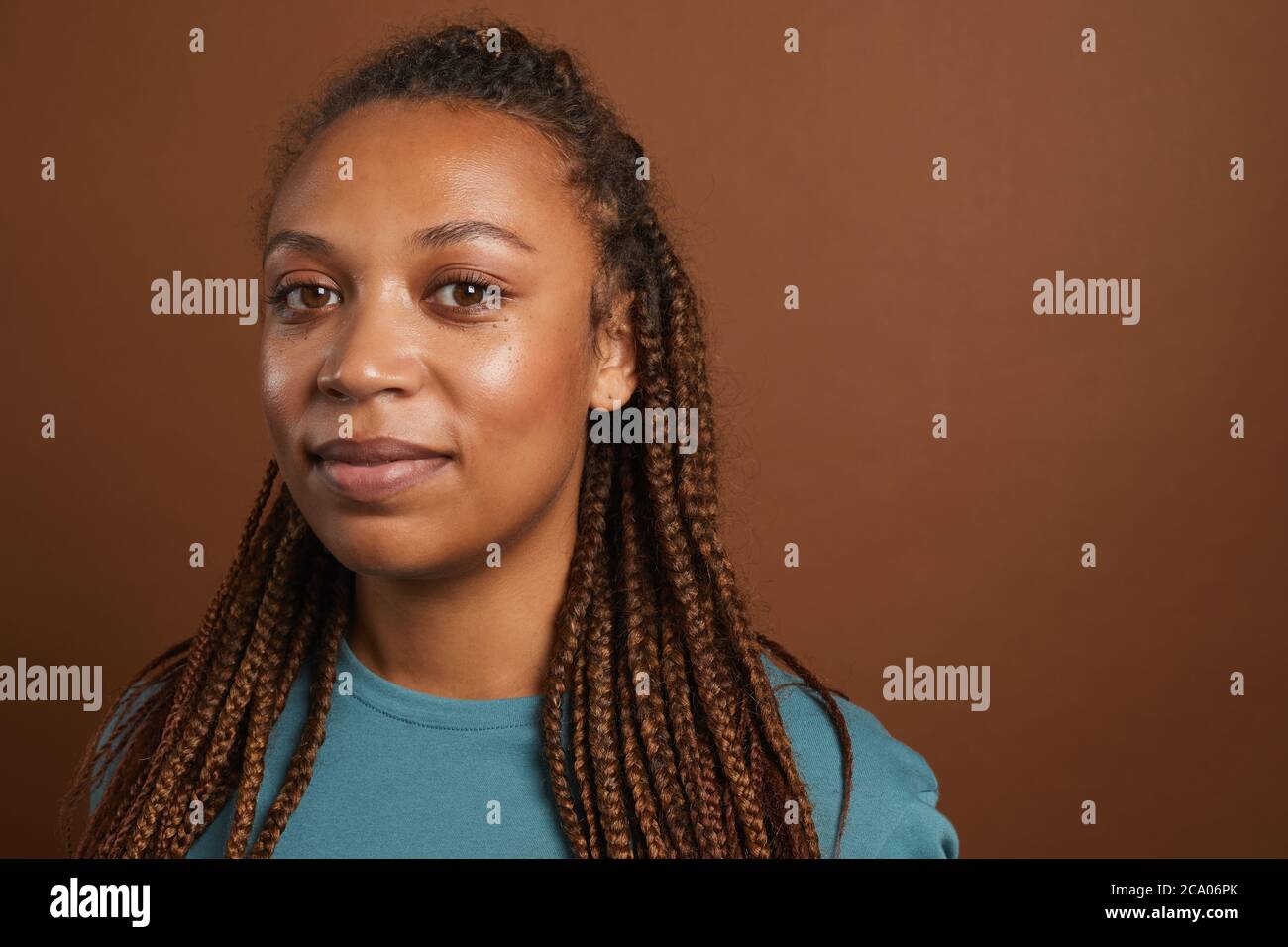 Minimales Kopf- und Schulterporträt einer modernen afroamerikanischen Frau, die vor der Kamera lächelt, während sie vor braunem Hintergrund im Studio steht, Kopierraum Stockfoto
