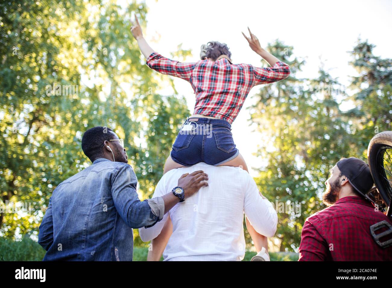 Rückseite des nicht erkennbaren gemischten Rennen verschiedene junge Menschen gehen in den Park am Sommernachmittag. Freund trägt seine Freundin auf Huckepack und Stockfoto