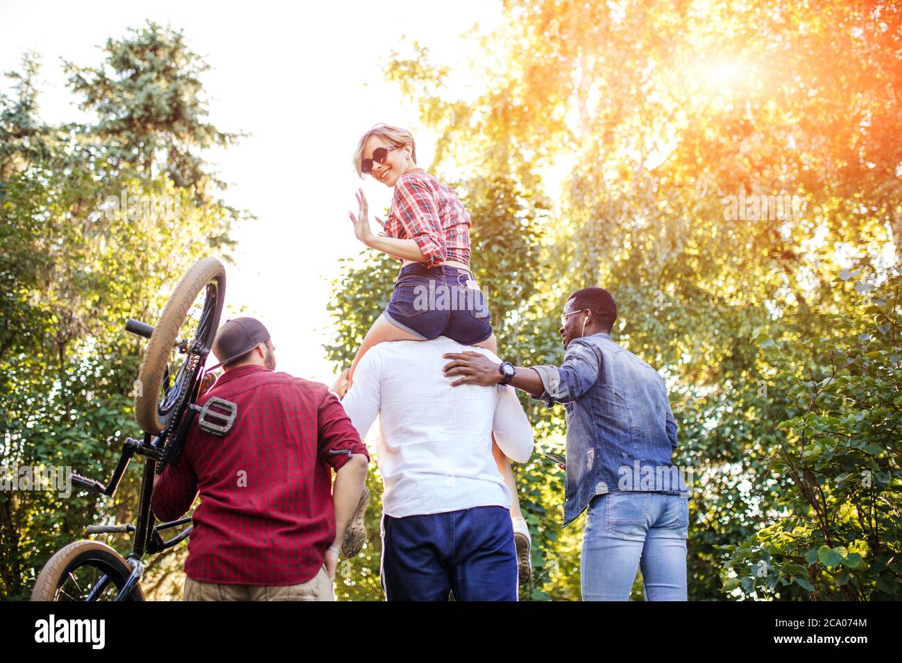 Rückansicht von nicht erkannten multirassischen Menschen, die am Sommernachmittag in den Park gehen. Freund trägt seine Freundin auf Huckepack und einer von Jungs Auto Stockfoto