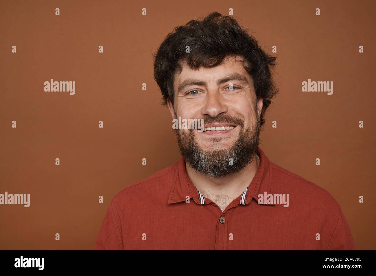 Minimal Kopf und Schultern Porträt von reifen bärtigen Mann lächelt an der Kamera, während vor braunem Hintergrund im Studio stehen, kopieren Raum Stockfoto