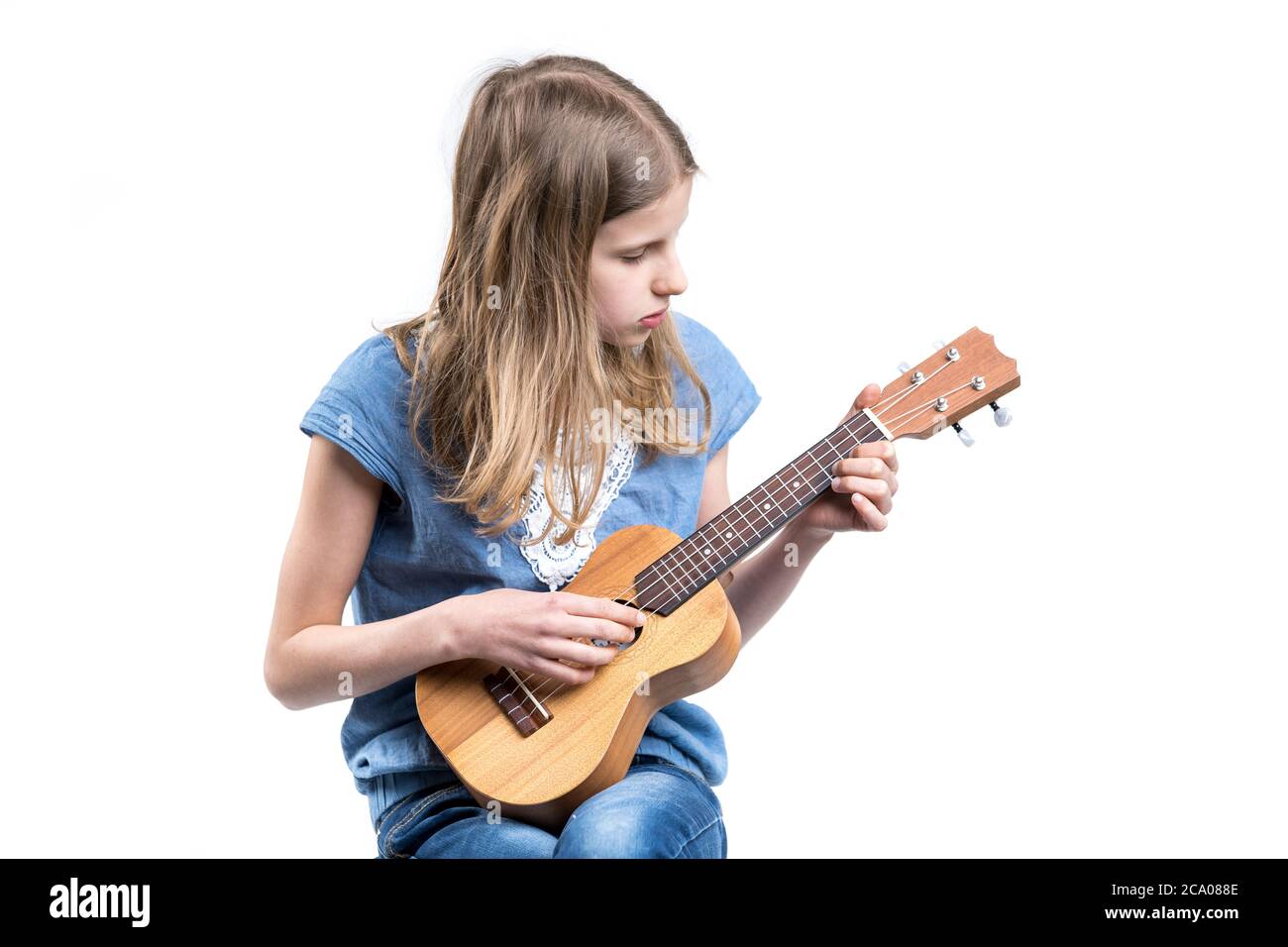 Junge, blonde Mädchen in blauem T-Shirt spielt Musik auf Ukulele-Instrument. Stockfoto