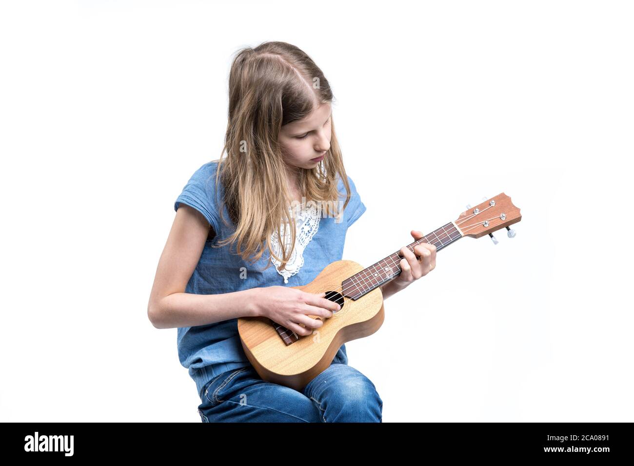Junge, blonde Mädchen in blauem T-Shirt spielt Musik auf Ukulele-Instrument. Stockfoto