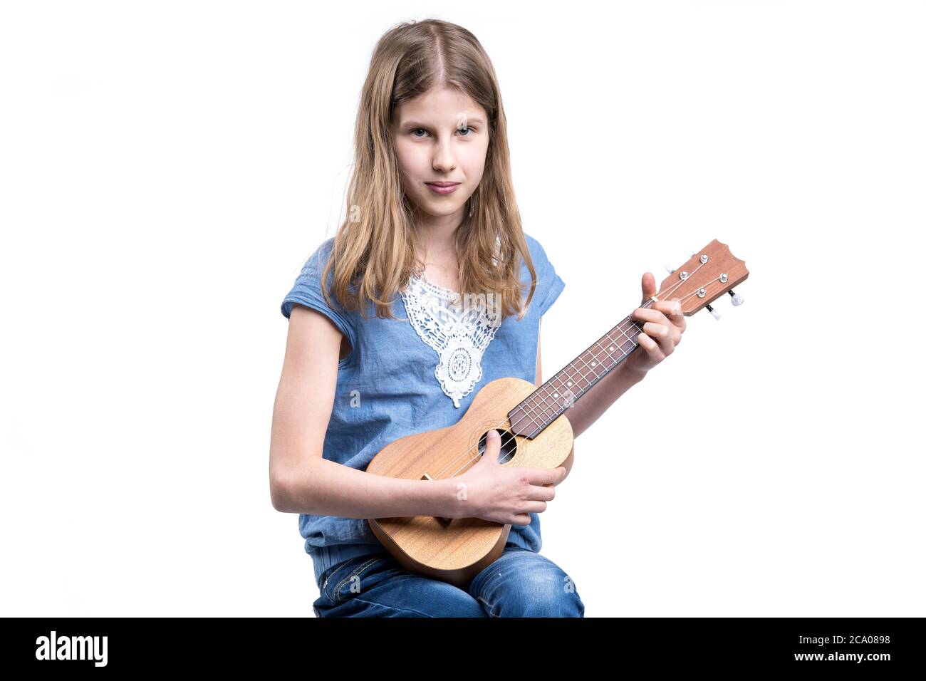 Junge, blonde Mädchen in blauem T-Shirt spielt Konzert auf Ukulele-Instrument. Stockfoto