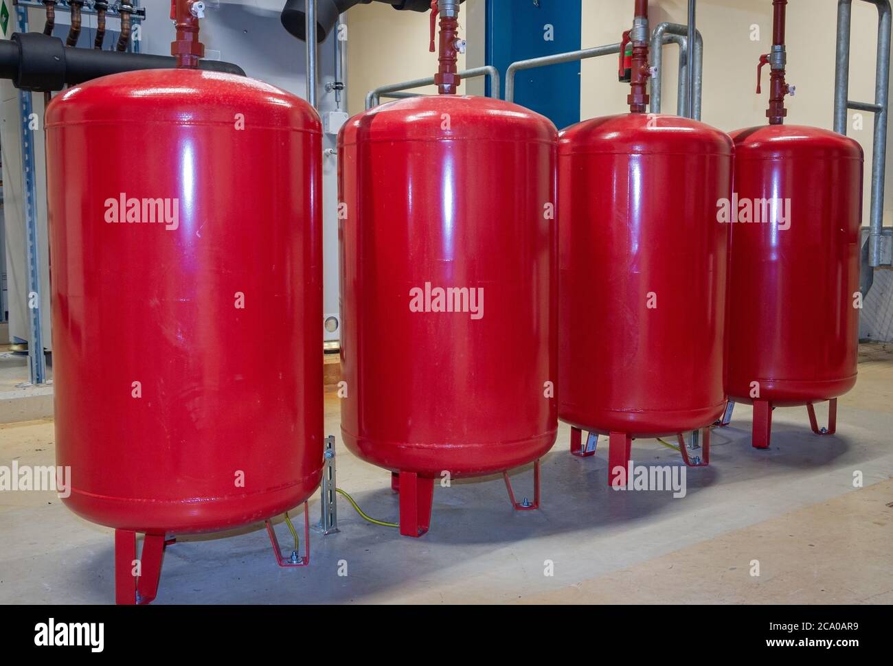 Leuchtend rote Ausdehnungsgefäße in einer Reihe in einem Zentralheizraum auf industrieller Ebene angeordnet Stockfoto