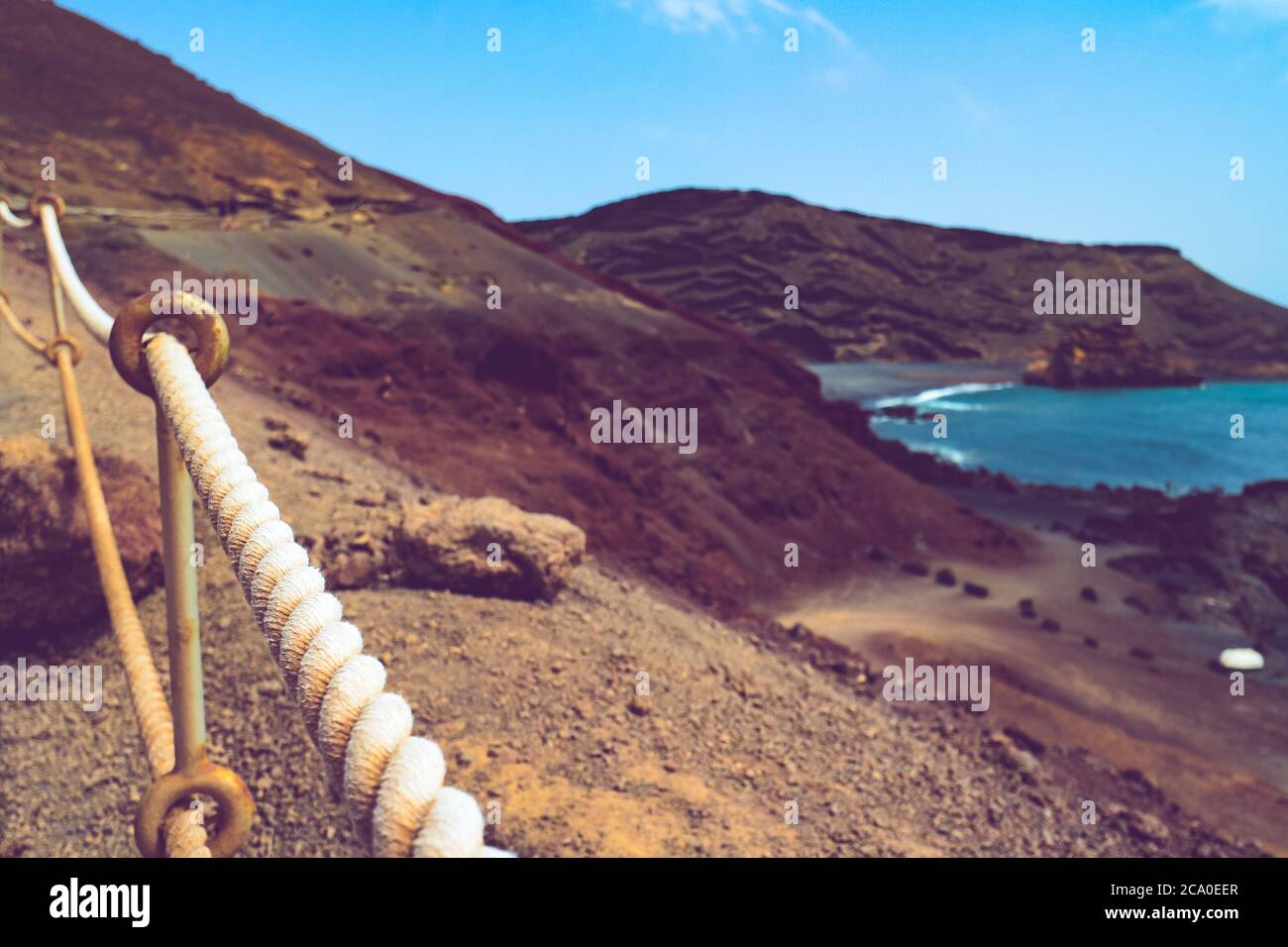 Seilgeländer an einer felsigen vulkanischen Küste mit roter Erde und schwarzem Sand am Atlantik in El Golfo, Lanzarote, Kanarische Inseln, Spanien. Stockfoto