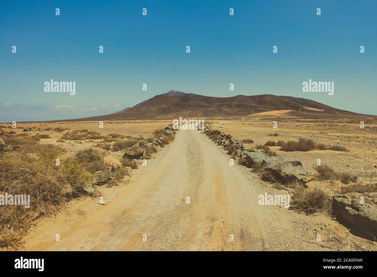 Einsame Wüstenstraße durch eine trockene Landschaft windet sich in Richtung vulkanischer Berge am Horizont, gesehen in der Rubicon Ebene in der Nähe von Playa Blanca, Lanzarote. Stockfoto