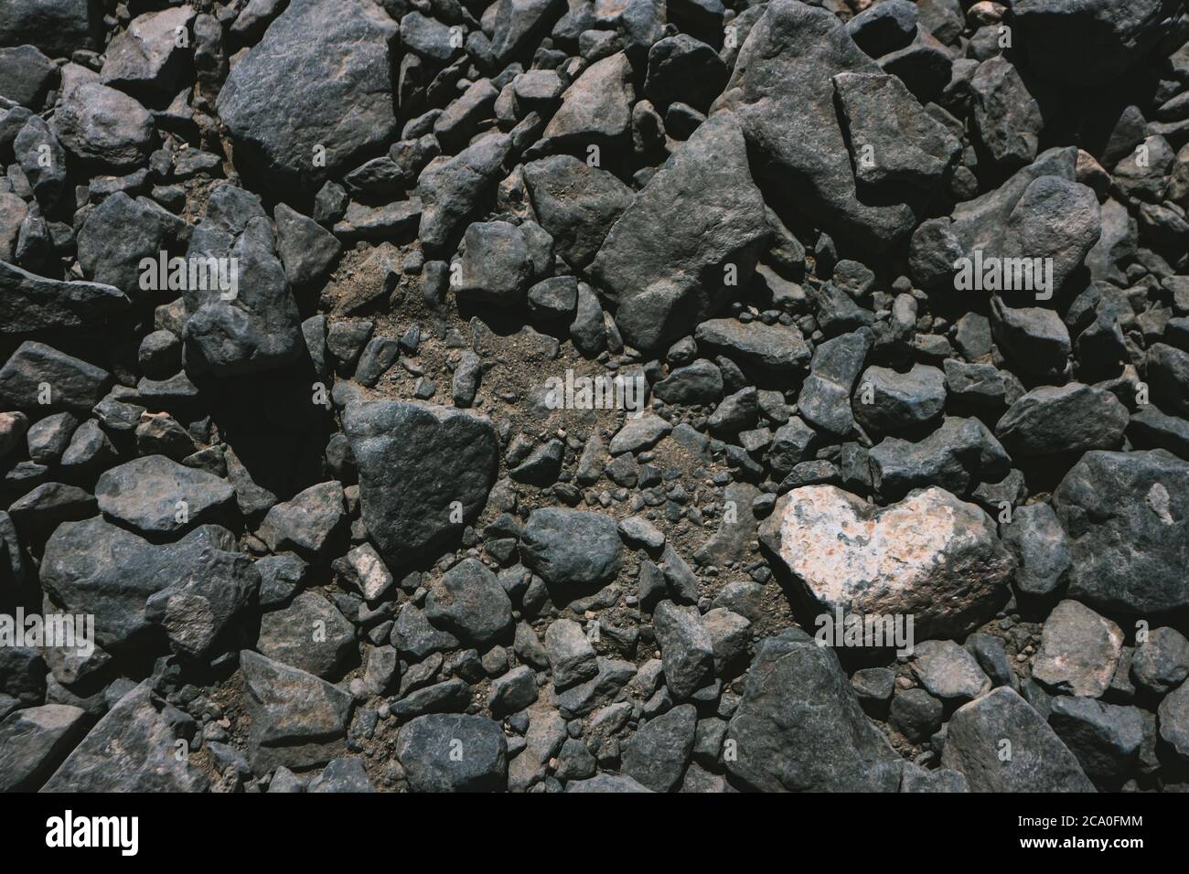Herzförmiger weißer Stein zwischen dunklen vulkanischen Felsen Hintergrund mit Kopierraum. Gesehen in Lanzarote, Kanarische Inseln, Spanien. Stockfoto