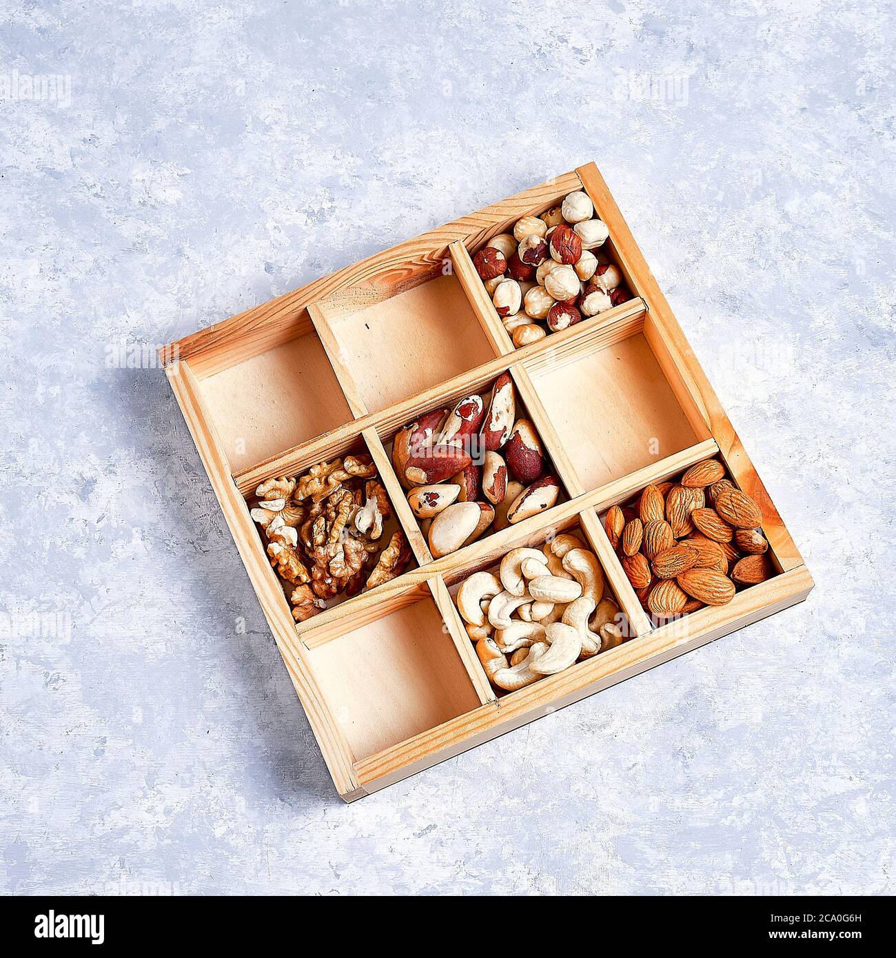 Pekannüsse, Haselnüsse, Mandeln, Kiefernnüsse, brasilianernuss, Cashews in einer Holzkiste auf blauem Grund, Draufsicht, flacher Lay Stockfoto