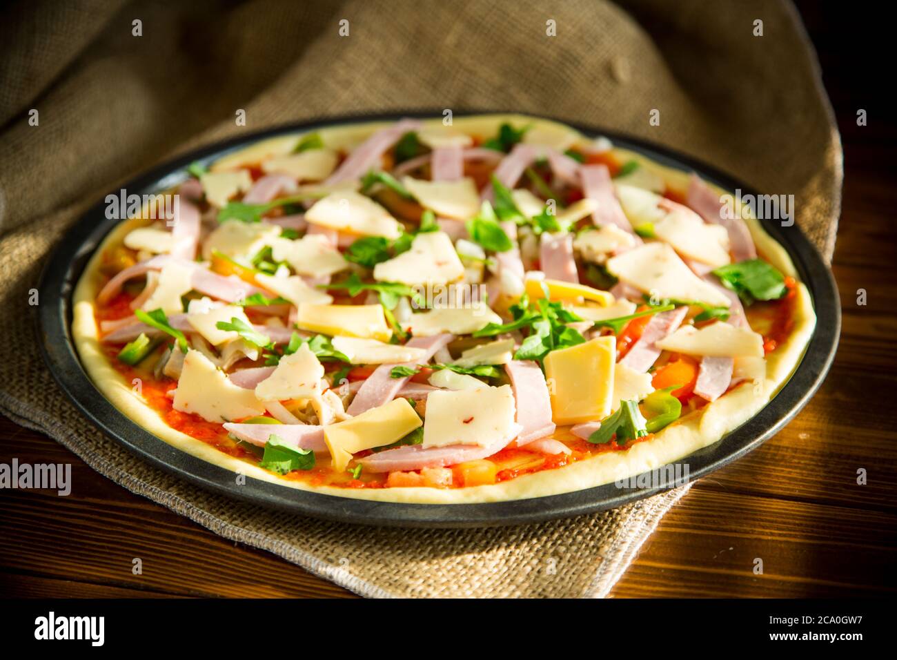 Rohe Pizza mit sortierter Füllung in Metallform auf einem Holztisch Stockfoto