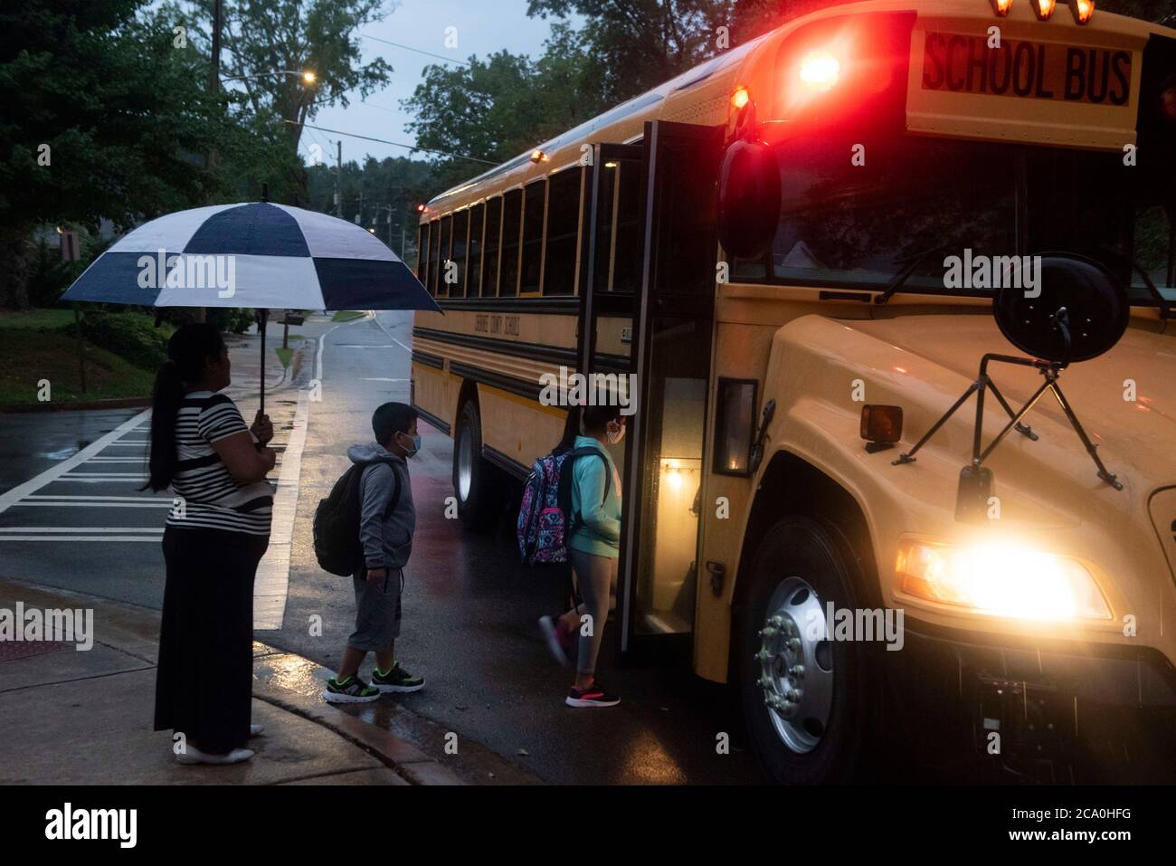 Kanton, GA, USA. August 2020. Grundschüler steigen im Regen in den Schulbus ein. Öffentliche Schulen in Cherokee County, GA, nördlich von Atlanta, haben am Montag wieder eröffnet, inmitten der Besorgnis der Mehrheit der Lehrer über angemessene Sicherheitsvorkehrungen gegen die Verbreitung von Covid-19-Infektionen. Das County-System ist eines von drei in der Atlanta U-Bahn-Bereich mit einem großen Prozentsatz der Studenten entscheiden sich für face-to-face-Klassen. Die meisten anderen Landkreise entschieden sich, mit virtuellem Lernen wieder zu öffnen. Quelle: Robin Rayne/ZUMA Wire/Alamy Live News Stockfoto