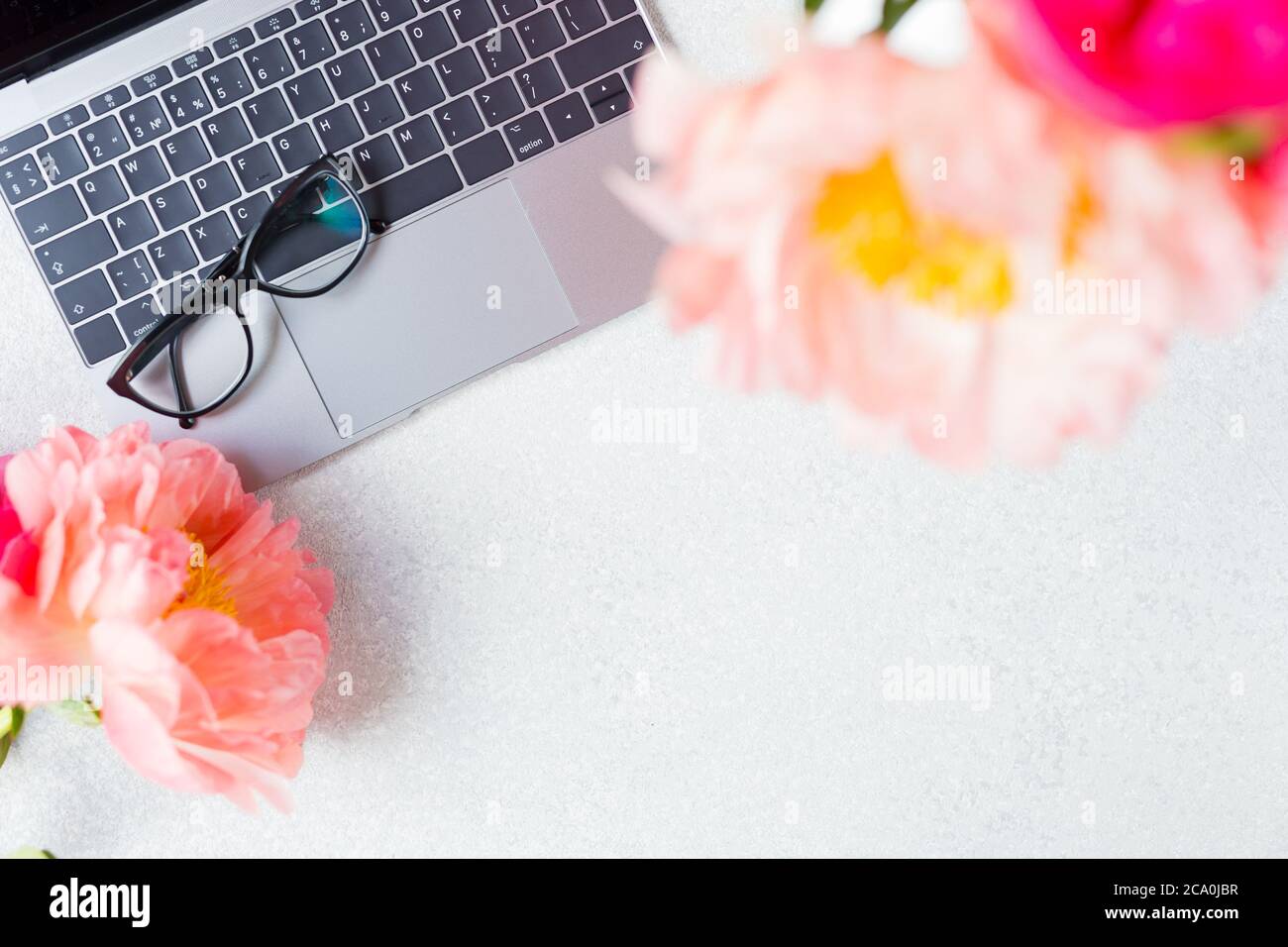 Arbeitsplatz, Desktop-Ansicht. Laptop, pinkfarbenes Pfingstrosen, Brille im Modell. Arbeitsplatz für Frauen. Speicherplatz kopieren. Stockfoto