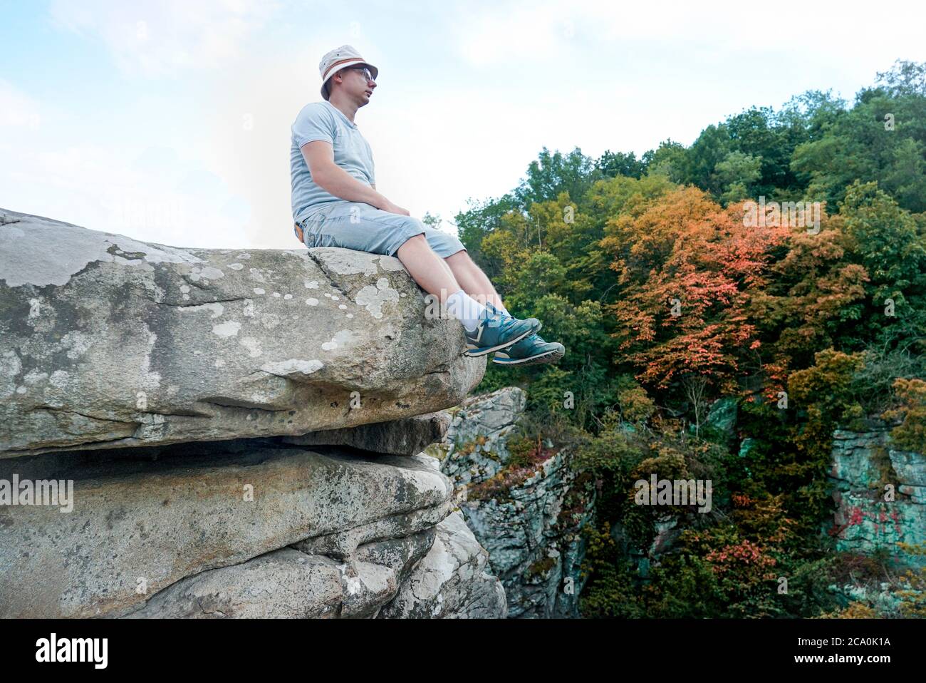 Ein Kerl sitzt auf einem Felsen in den Bergen auf einem Stein, gekleidet in ein T-Shirt und Shorts Stockfoto