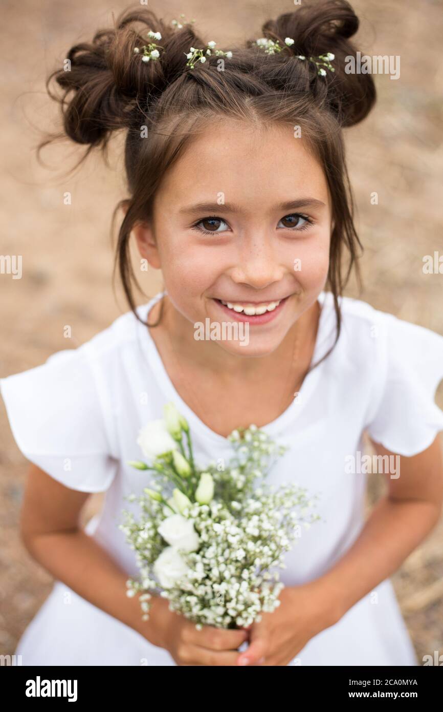 Ein Mädchen hält einen Strauß weißer Blumen auf einem verschwommenen Hintergrund.dunkles Haar, weiße Blumen in den Händen, weißes Kleid Stockfoto