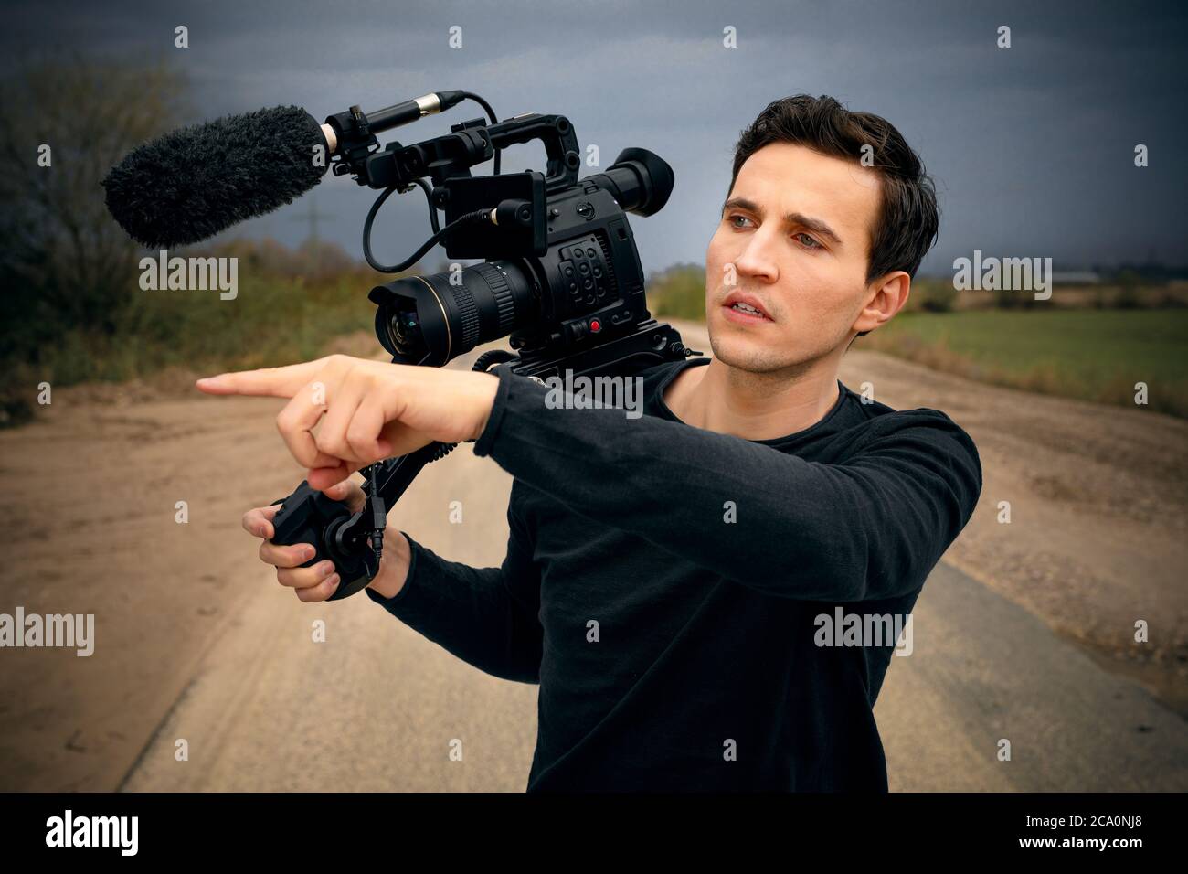 Junger männlicher Kameramann gibt Anweisungen an jemanden mit Finger zur Seite und Kamera und seine Schulter beim Videodreh Stockfoto