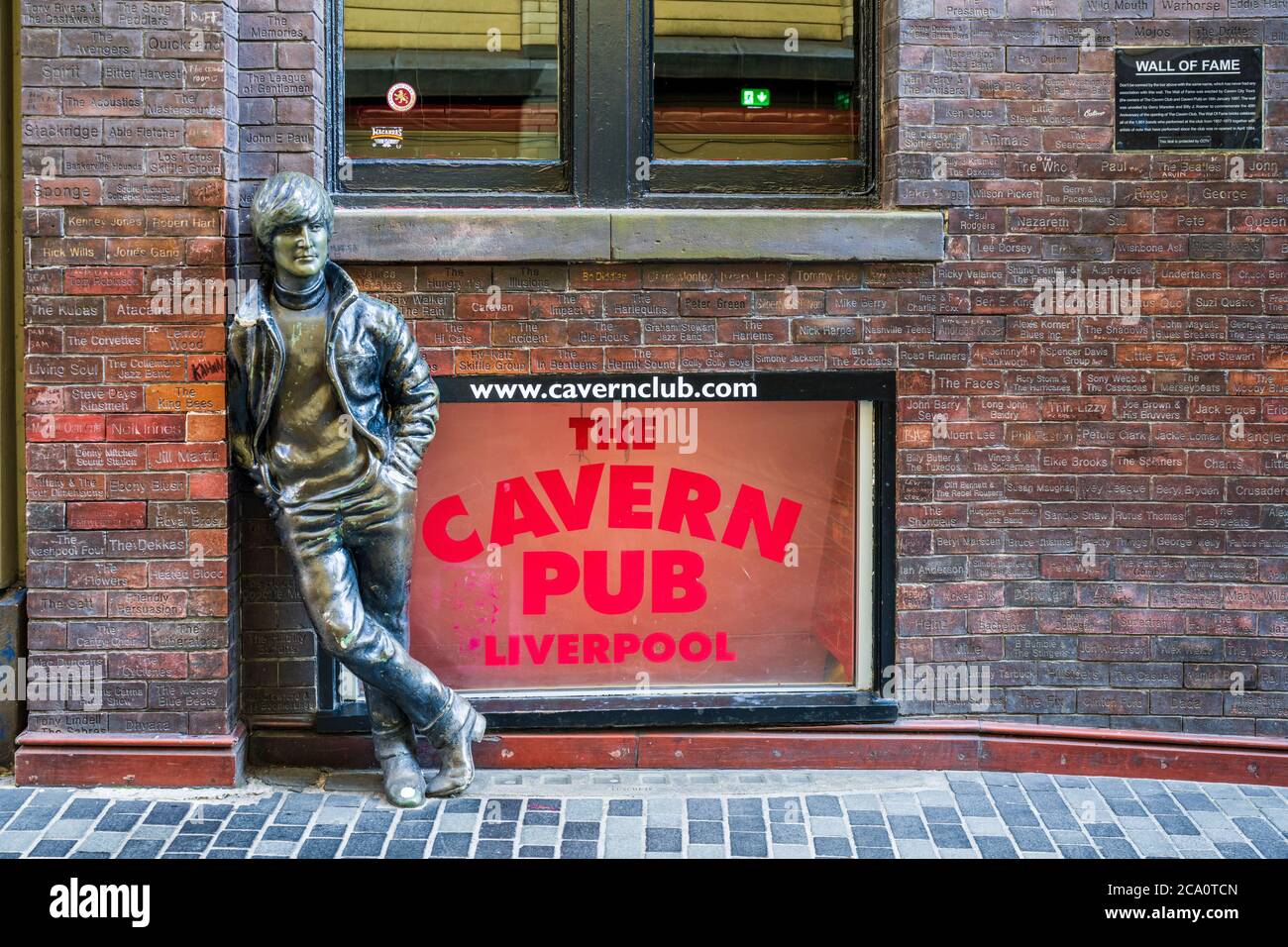 John Lennon Statue Mathew Street Liverpool in der Nähe des Cavern Club. Wall of Fame zeigt die Namen von Künstlern, die im Cavern Club spielten. Cavern Pub. Stockfoto
