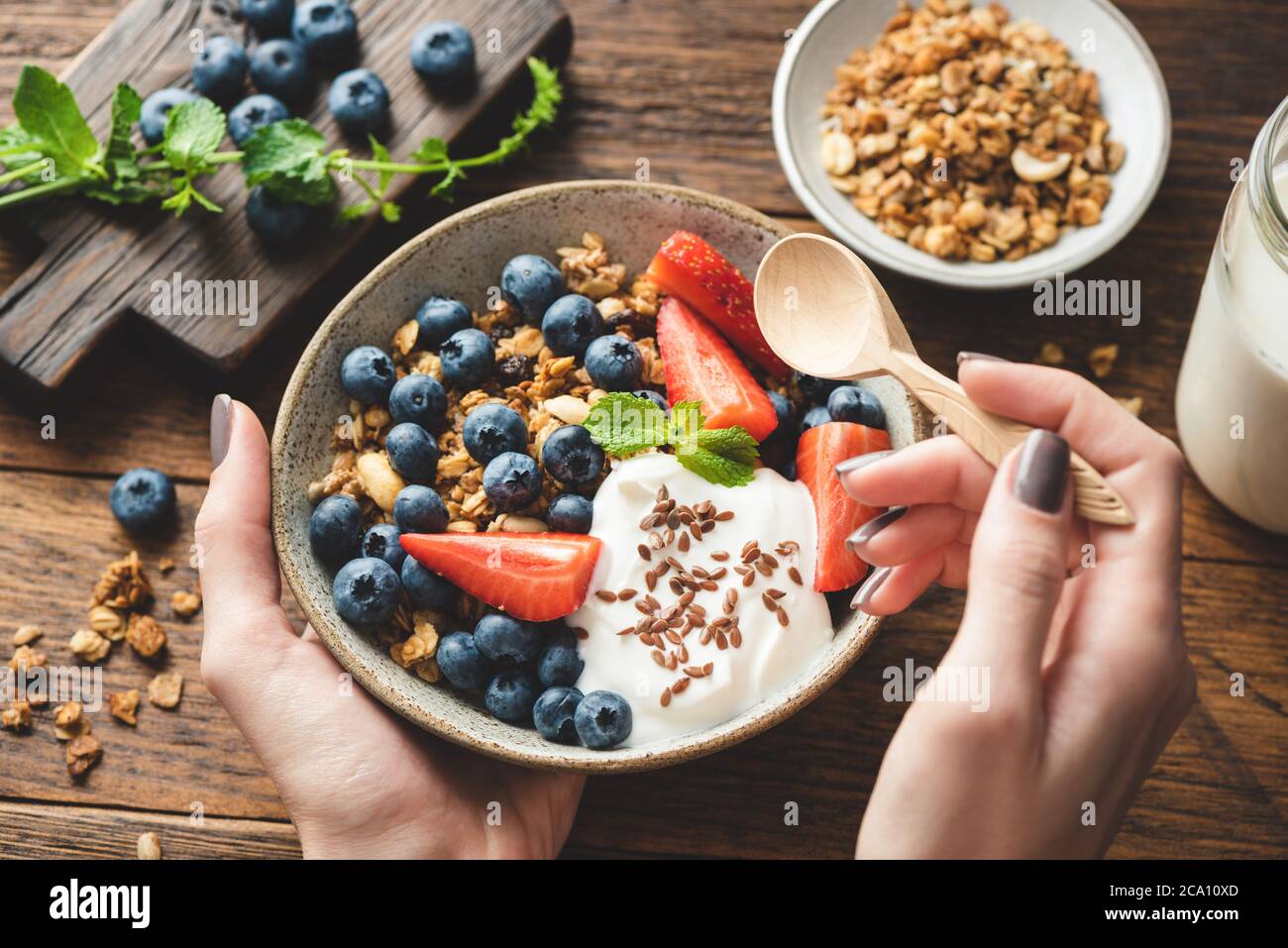 Essen Müsli mit griechischem Joghurt und Beeren. Weibliche Hände halten Schüssel mit gesunden Frühstücksflocken Müsli mit Obst und Joghurt. Konzept der Reinigung Stockfoto