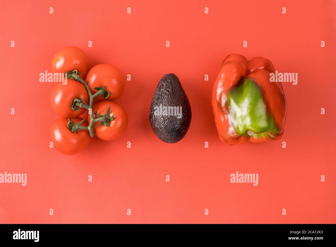 Layout aus Avocado, Tomaten und Pfeffer. Food-Konzept. Gemüse auf rotem Hintergrund. Minimales Sommerkonzept. Gemüsedesign. Stockfoto