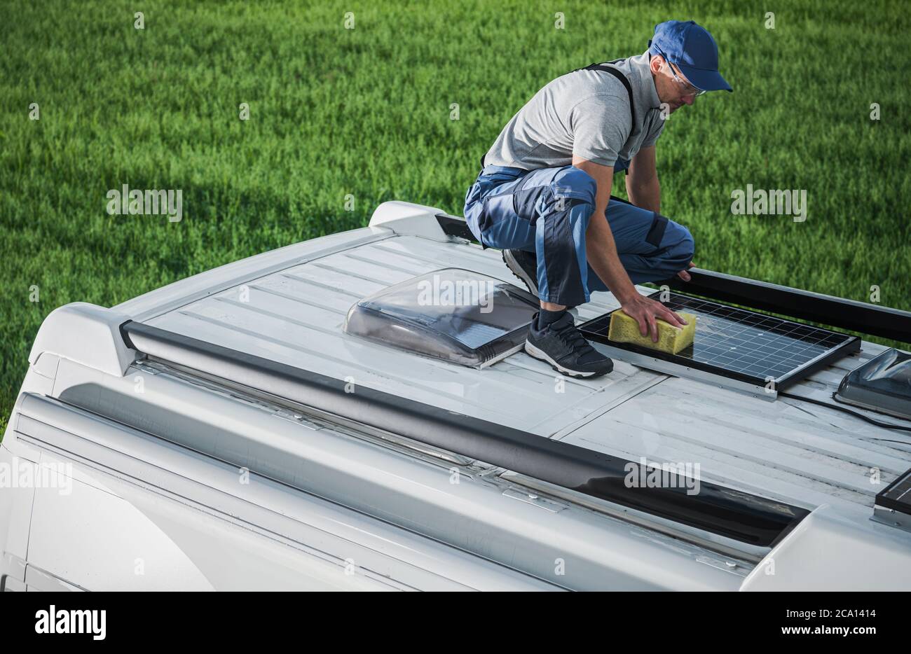 Kaukasische Männer in seinen 40er Jahren Reinigung Camper Van RV Dach installiert Sonnenkollektoren mit Schwamm und weichen Waschmittel. Wartung Des Wohnmobils. RV Industr Stockfoto