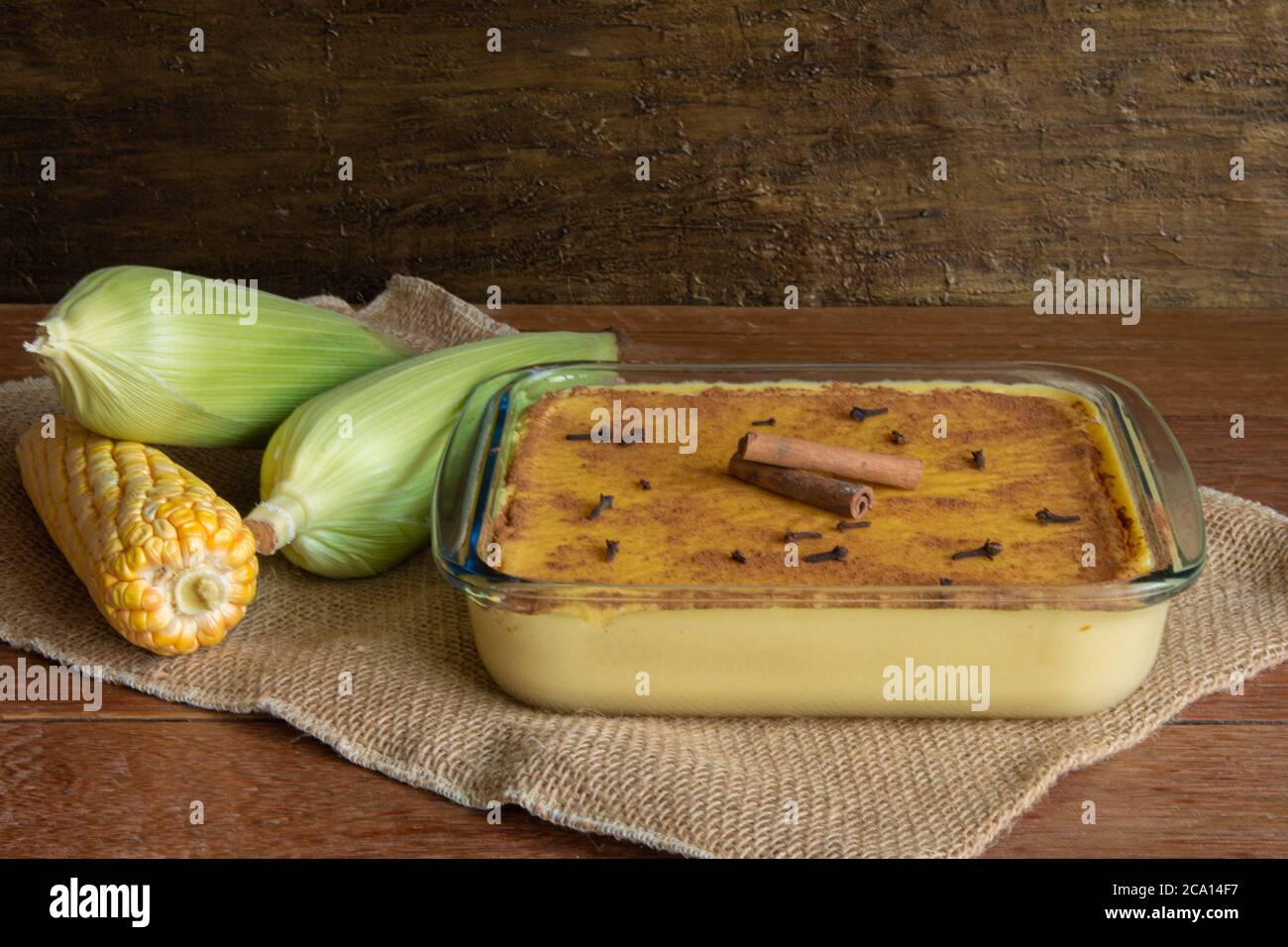Canjica Curau. Typische brasilianische Junina Party Süßigkeiten. Maiskolben. Rustikaler Holzhintergrund. Brasilianisches Dessert Stockfoto