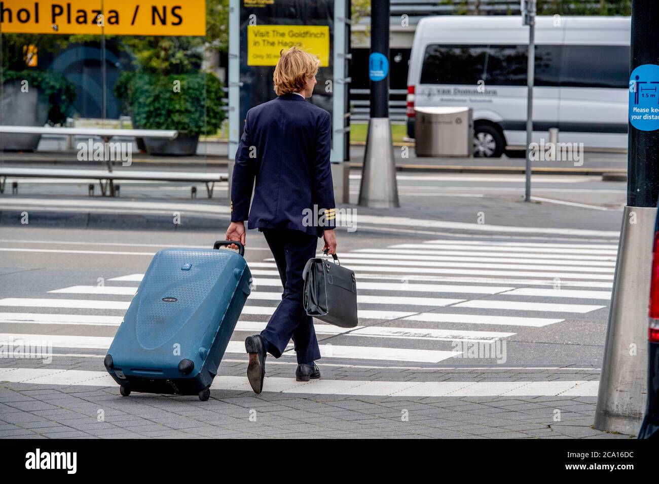 Ein KLM-Steward mit seinem Gepäck läuft während der Coronavirus-Krise am  Flughafen Schiphol.Es ist wieder Geschäft am Flughafen Schiphol, da die  Leute während der Sommerferien jedoch mit obligatorischer Gesichtsmaske  reisen. Die Fluggesellschaft KLM