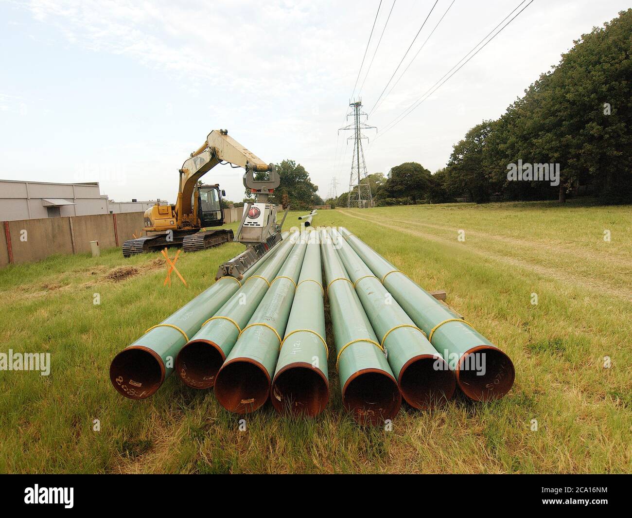 Rohre warten darauf, einer Pipeline hinzugefügt werden, die eine Bohrstelle mit einem Netz von Pipelines verbindet, die das Erdgas in Kraftwerke bringen. Die Pipeline verläuft unter Stromleitungen, die aus dem Erdgas hergestellt werden. Stockfoto