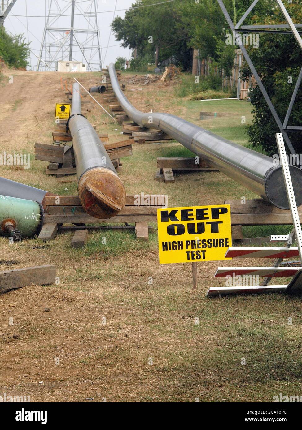 Rohre warten darauf, einer Pipeline hinzugefügt werden, die eine Bohrstelle mit einem Netz von Pipelines verbindet, die das Erdgas in Kraftwerke bringen. Die Pipeline verläuft unter Stromleitungen, die aus dem Erdgas hergestellt werden. Stockfoto