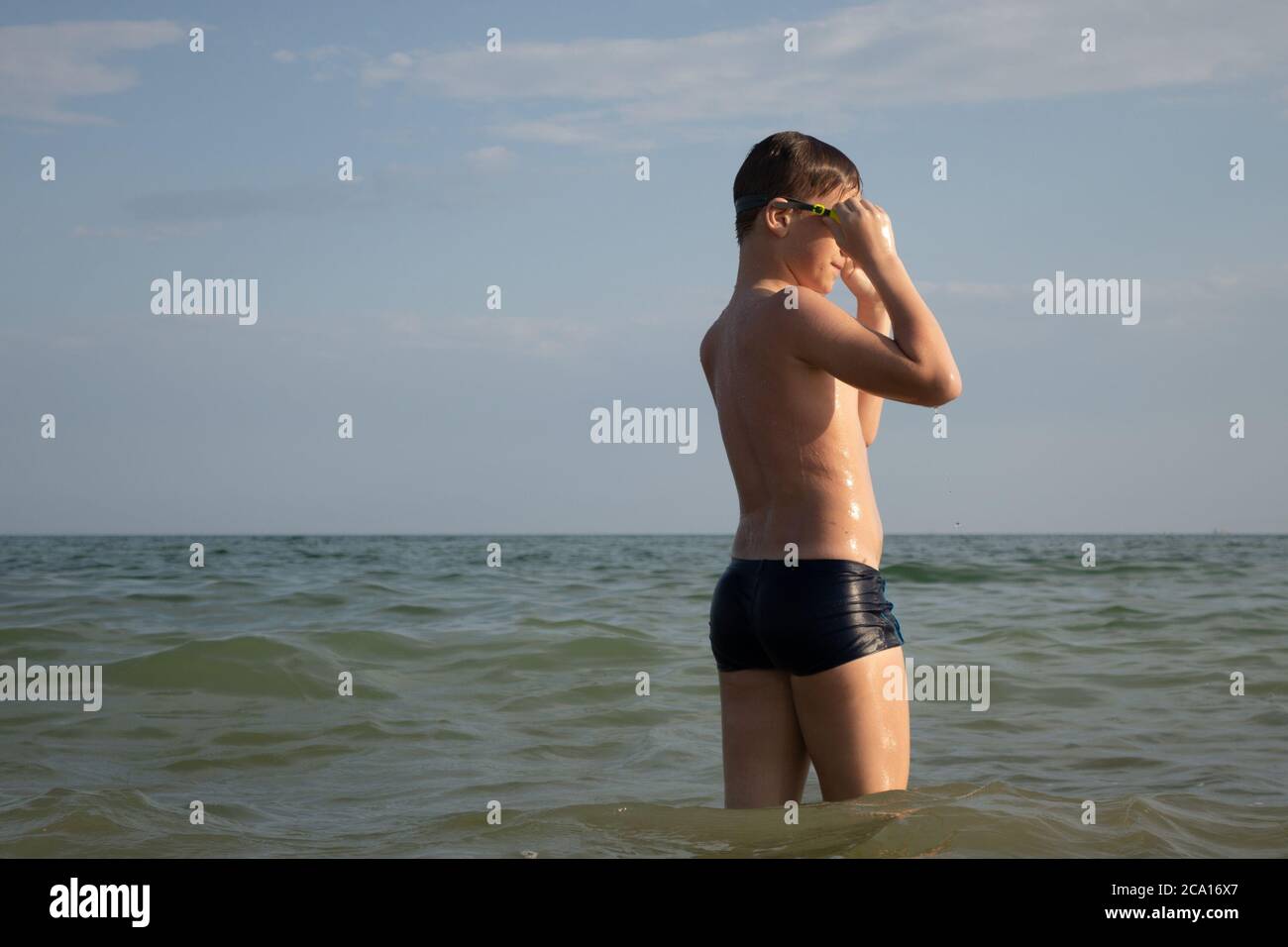 Ein 10-jähriger Junge zieht eine Schwimmbrille an und bereitet sich auf das Schwimmen im Meer vor. Stockfoto