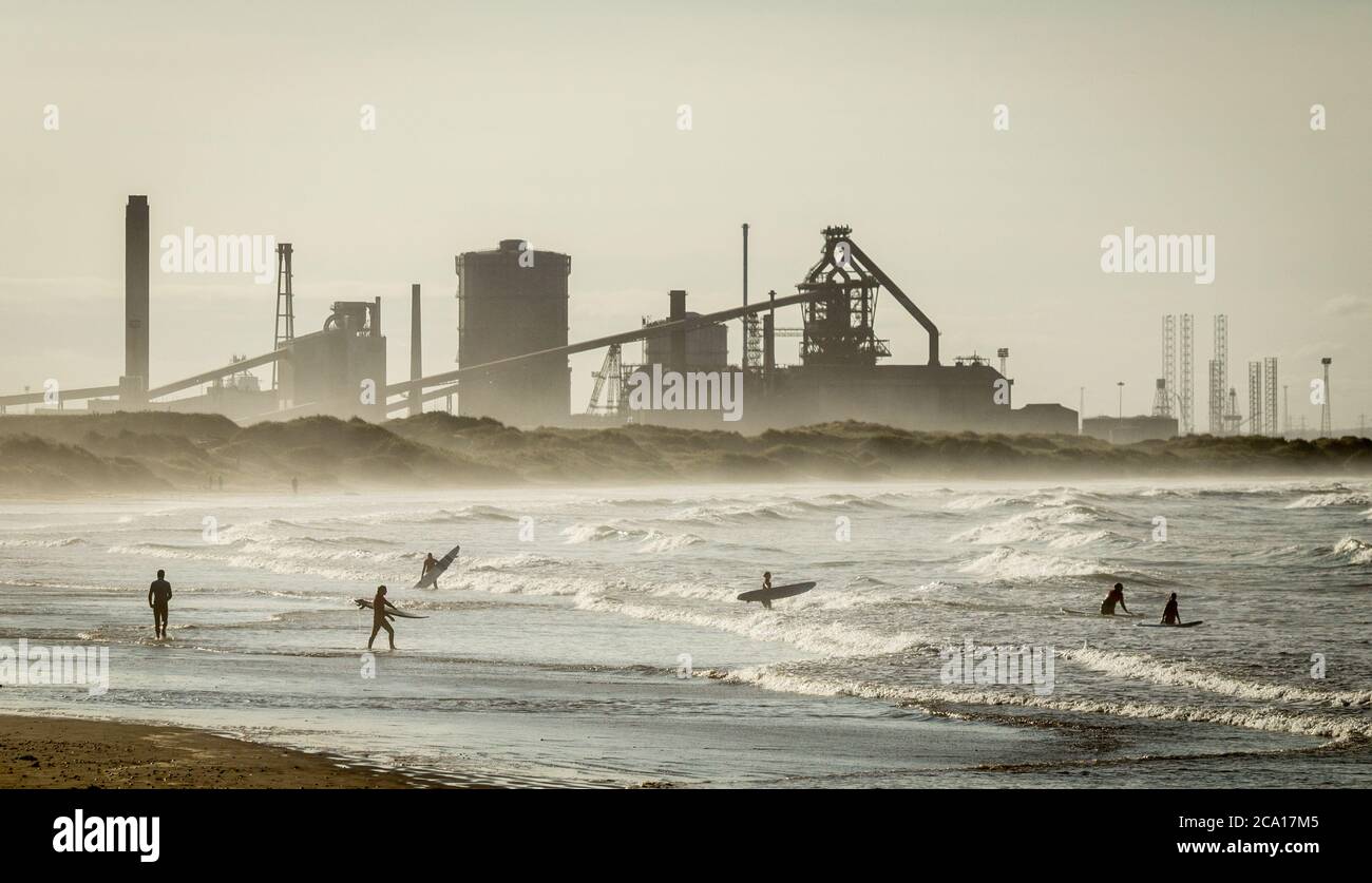 Surfer fahren vom Redcar Strand mit Redcar Stahlwerk im Hintergrund. Stockfoto