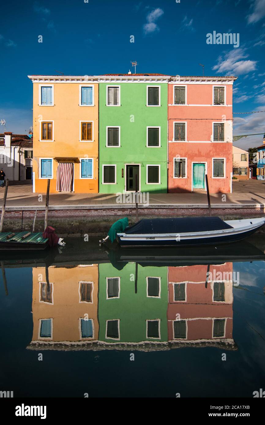 Typische bunte Häuser der Insel Burano spiegeln sich auf einem venezianischen kanal mit einem Boot Stockfoto