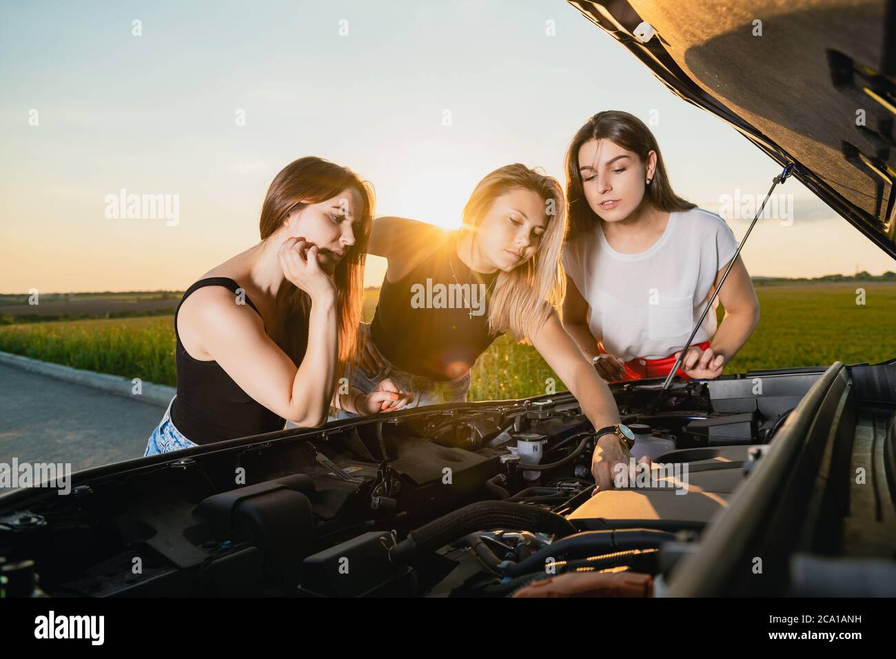 Drei Freundinnen hatten Probleme während der Fahrt aus der Stadt, öffnen Sie die Motorhaube, um die Details zu überprüfen und versuchen, sich zu beruhigen Stockfoto