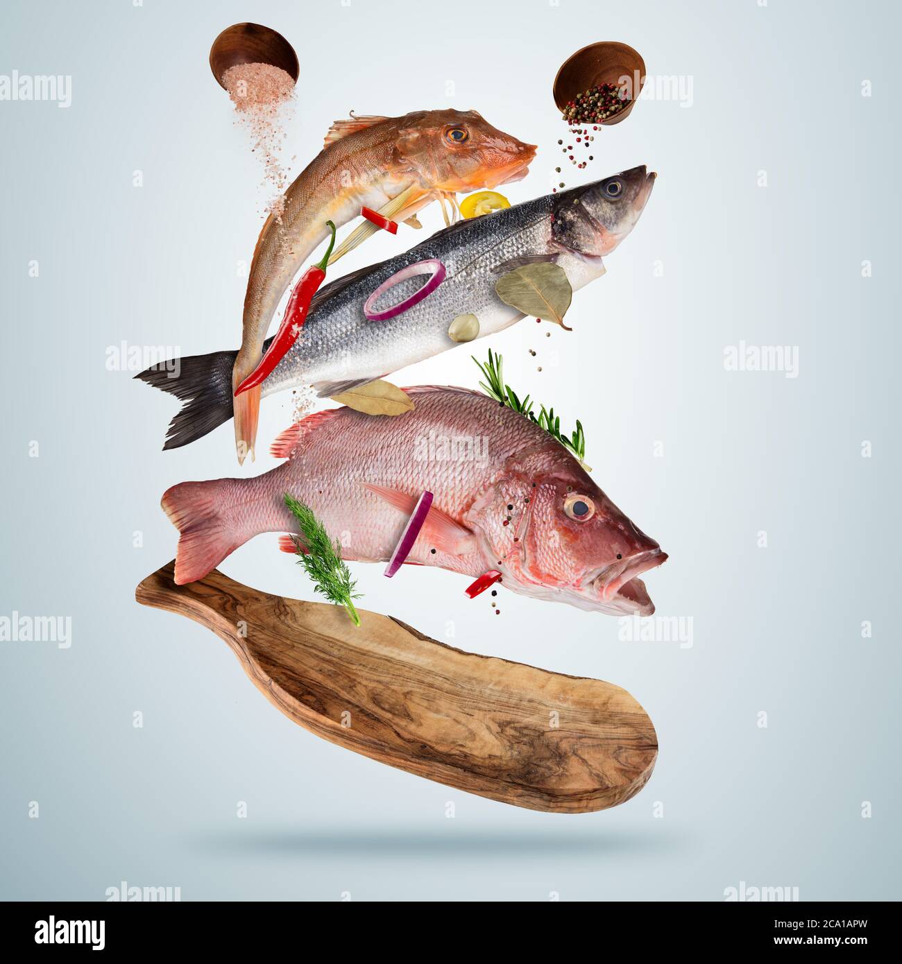 Frischer Seefisch mit fallenden Gewürzen, fliegend über Holzbrett, isoliert auf grauem Hintergrund. Zubereitung von Speisen, frische Mahlzeit bereit zum Kochen. Extra hoch Stockfoto