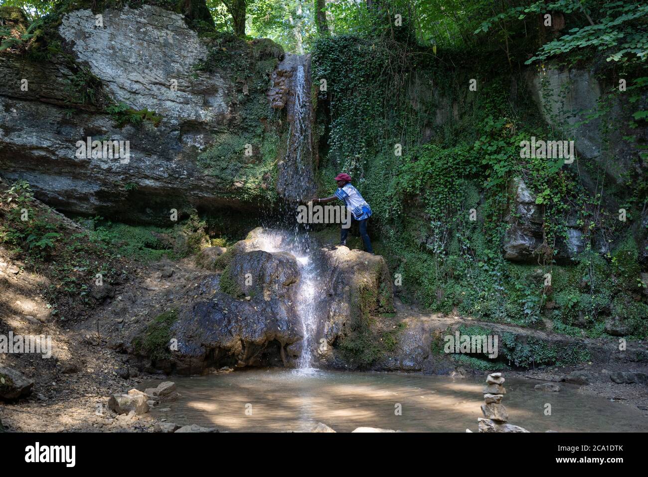 Afrikanische Frau steigt an einem heißen Tag im Sommer auf das Wasser eines Wasserfalls. Der Linner Wasserfall ist der größte Wasserfall des Kantons Aargau und liegt bei Sag Stockfoto