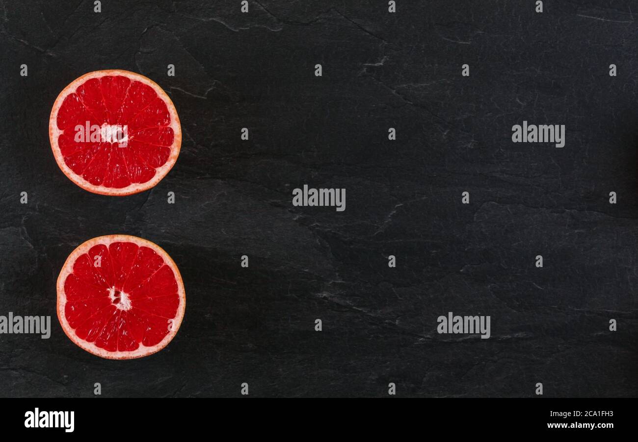 Rosa Grapefruit halbiert auf schwarzem Schiefertafel Foto von oben. Breites Banner mit Platz für Text rechts. Stockfoto