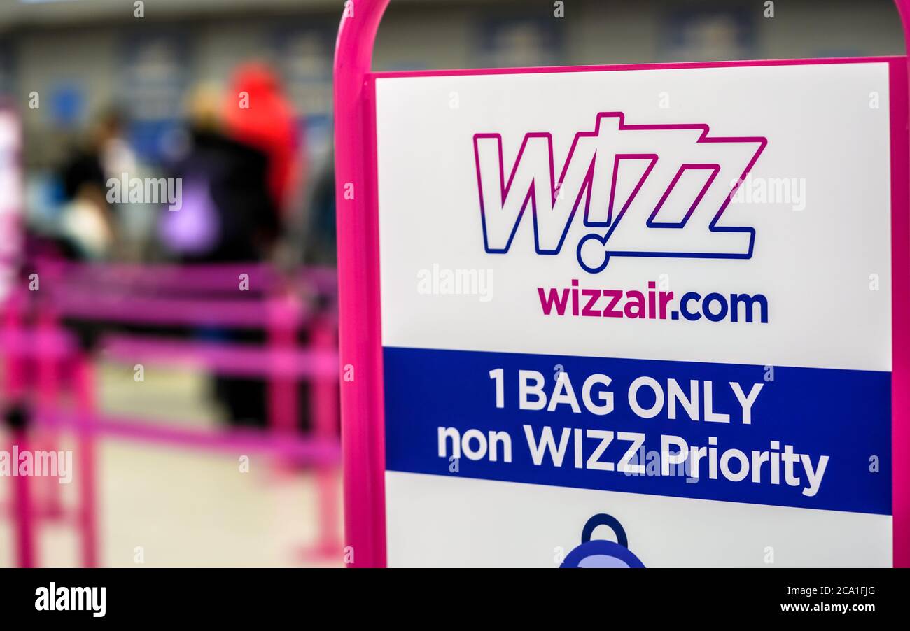 London, Großbritannien - 05. Februar 2019: Wizzair-Infotabelle über die maximale Gepäckgröße, verschwommene Personen an den Check-in-Schaltern im Hintergrund Wizz ist aufgehängt Stockfoto