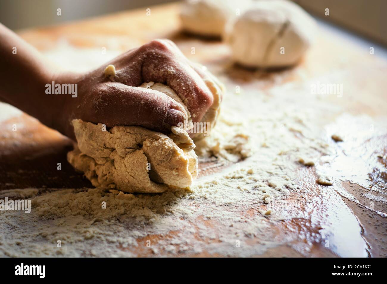 Weibliche Hand Kneten eines Mehlteigs durch Rollen auf einem Holzbrett. Zubereitung von Mehl-basierte Lebensmittel wie Brot oder Pizza Stockfoto